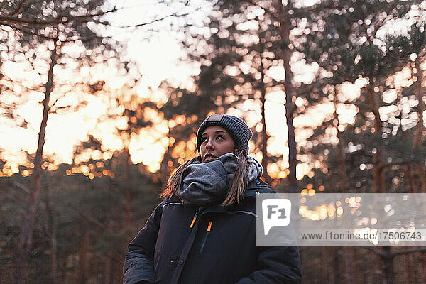 Young woman with warm clothing in forest at sunset
