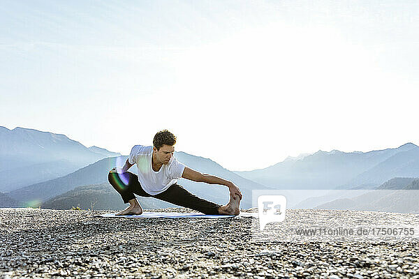 Flexible man practicing Skandasana with mountain view