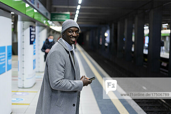 Smiling businessman with smart phone standing at railroad platform