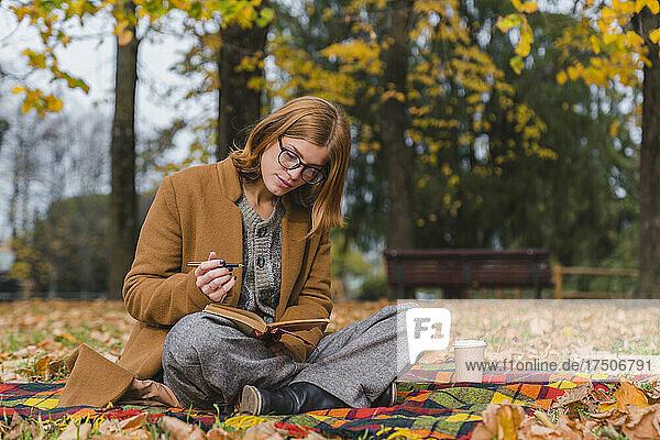 Woman with pen reading book in autumn park