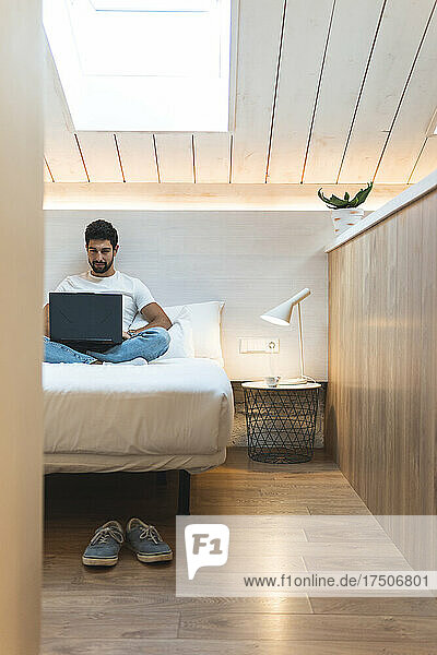 Geschäftsmann benutzt Laptop auf Bett im Dachboden zu Hause