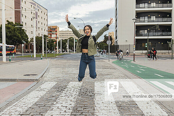 Sorglose Frau mit ausgestreckten Armen springt auf der Straße