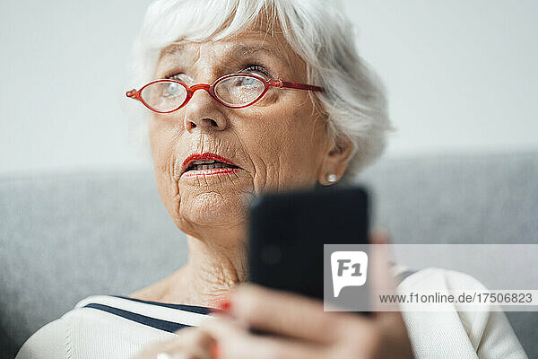 Woman with eyeglasses holding mobile phone at home