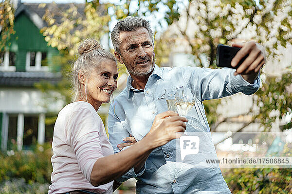 Smiling man taking selfie with woman through mobile phone at backyard