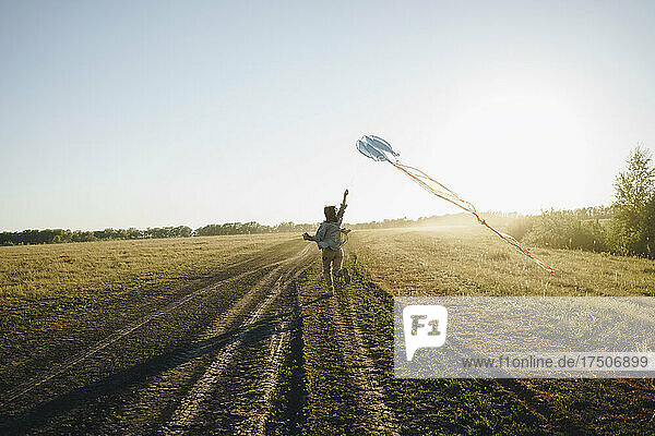 Woman with kite running on agricultural field