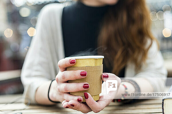 Woman with painted nails holding disposable coffee cup