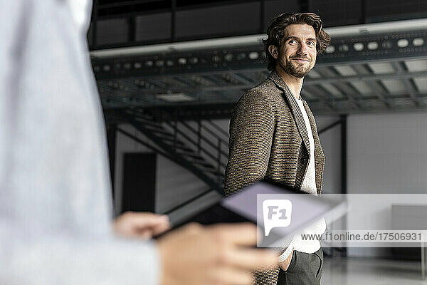 Smiling businessman looking at colleague with digital tablet in industrial hall