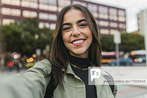 Smiling young woman taking selfie in city