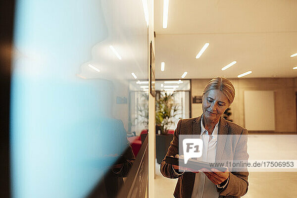 Businesswoman using tablet PC by screen in office