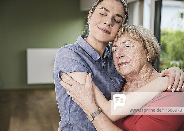 Women with eyes closed hugging each other at home