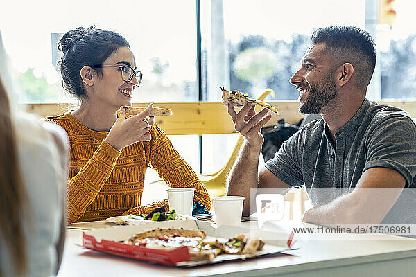Lächelnder Geschäftsmann isst Pizza mit Geschäftsfrau in der Mittagspause