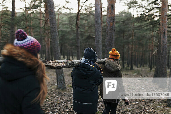 Friends carrying log on shoulders in forest