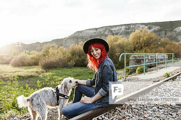Smiling woman stroking dog sitting on railroad track
