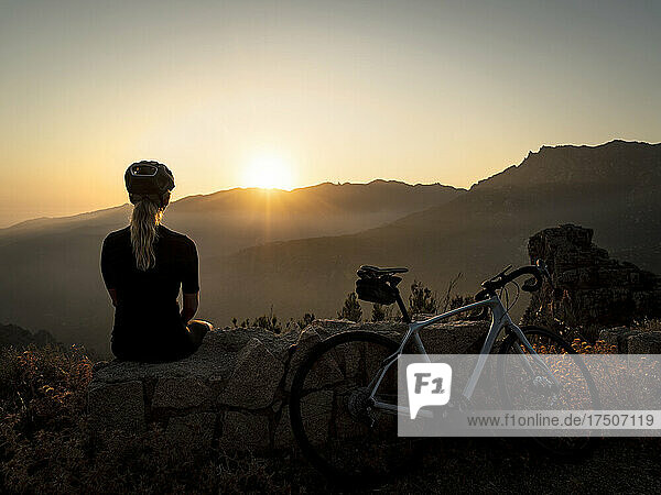Sportswoman sitting on rock and looking at sunset