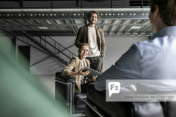 Smiling businessman and businesswoman discussing with colleague in industrial hall