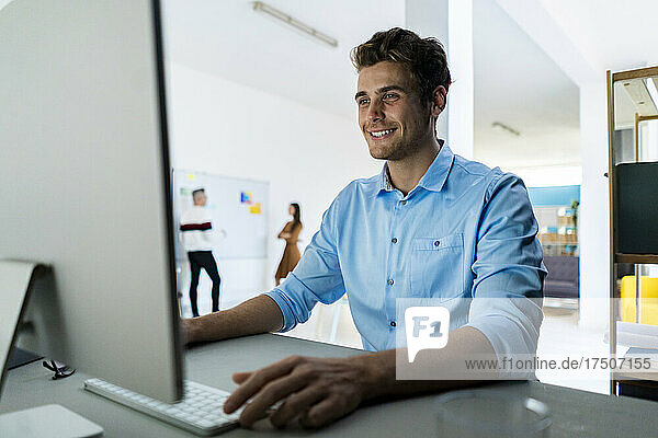 Smiling businessman working on desktop PC in office