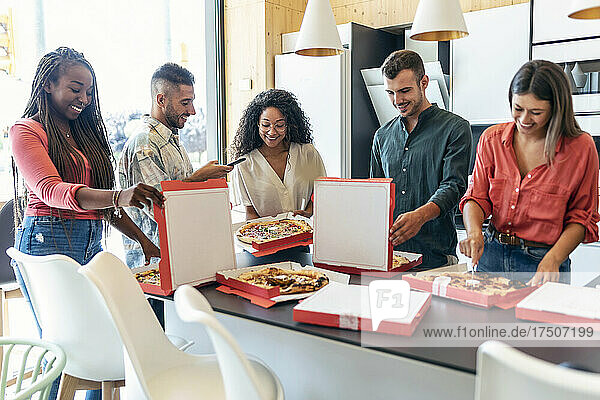 Glückliche  gemischtrassige Kollegen  die in der Bürokantine Pizza essen