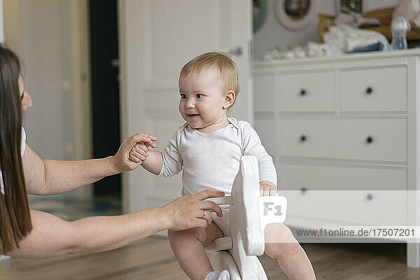 Mother assisting daughter sitting on rocking horse at home