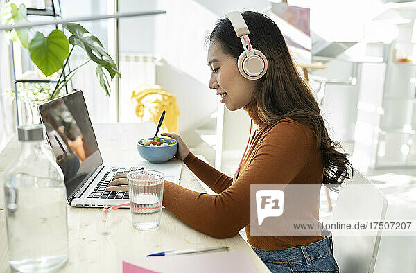 Young businesswoman with headphones using laptop at home office