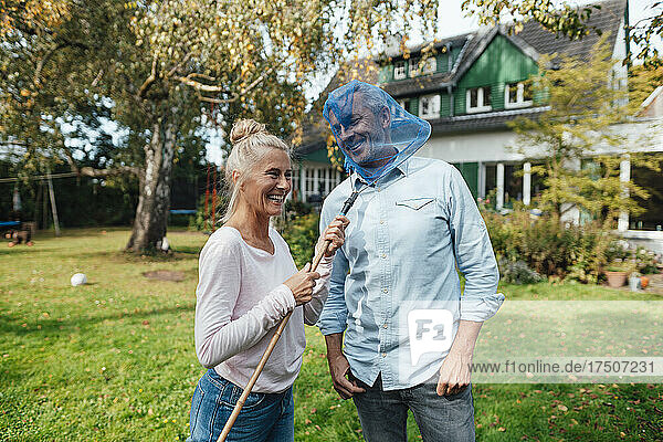 Smiling woman covering man face with butterfly fishing net at backyard
