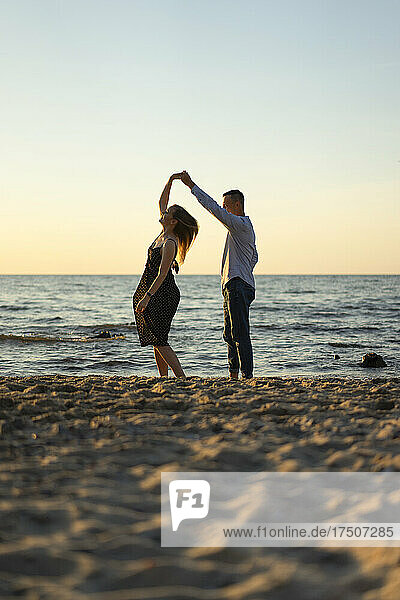 Young couple dancing together on sand at sunset