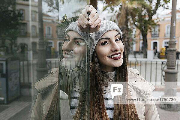 Young woman with brown hair leaning on glass wall in city