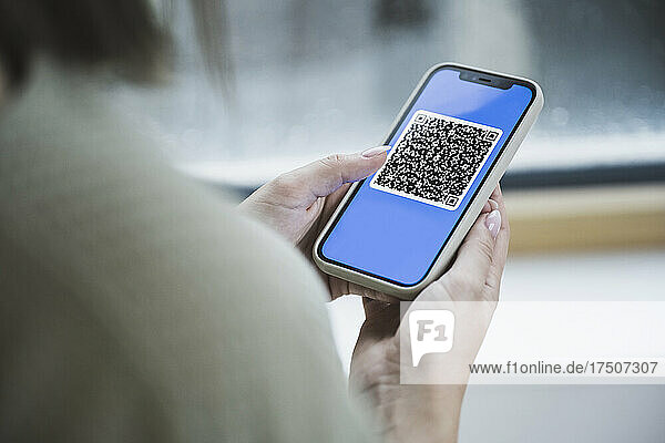 Woman holding mobile phone with QR code on screen