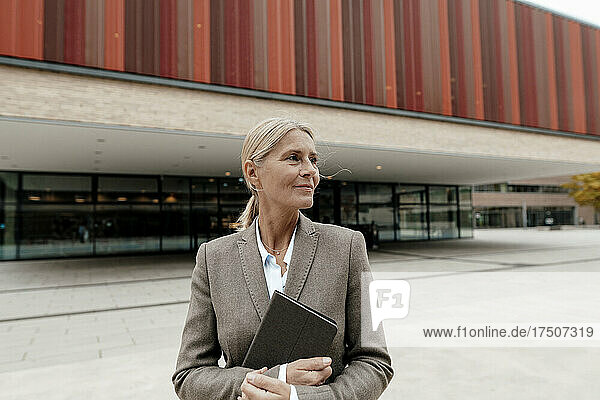 Blond businesswoman holding tablet PC on footpath