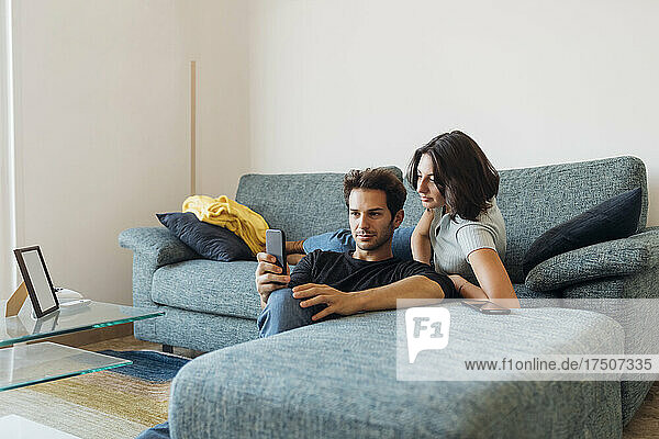 Young couple taking selfie through smart phone in living room at home