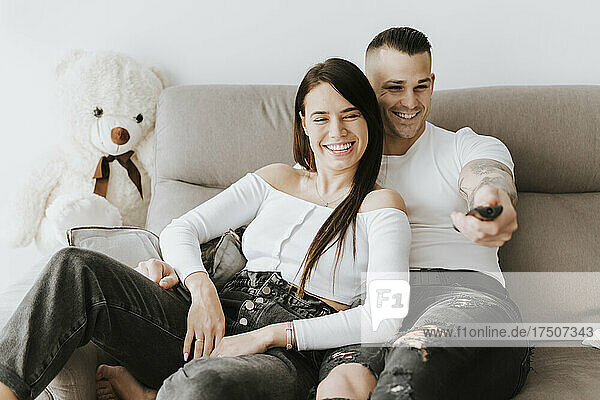 Smiling man holding remote watching TV with woman on sofa