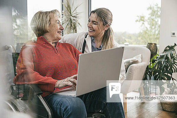 Disabled woman with laptop looking at nurse by wheelchair