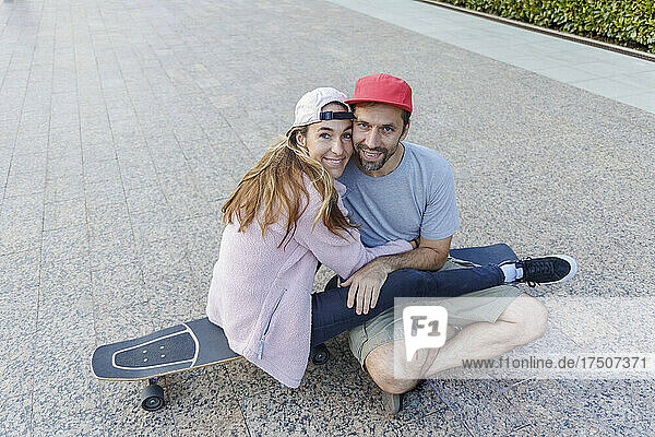 Woman embracing boyfriend sitting on skateboard at footpath