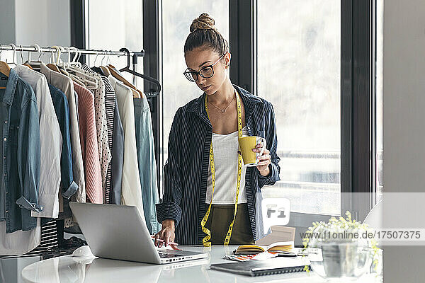 Modedesigner mit Kaffeetasse und Laptop im Büro