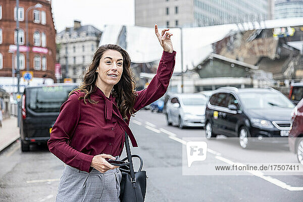 Businesswoman with hand raised hailing taxi on city street