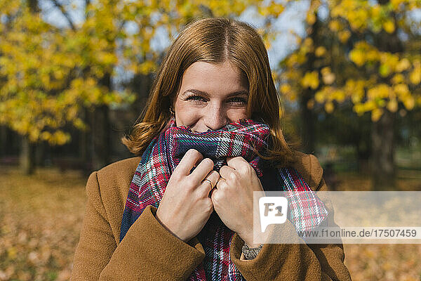 Glückliche Frau bedeckt Mund mit Stola im Park