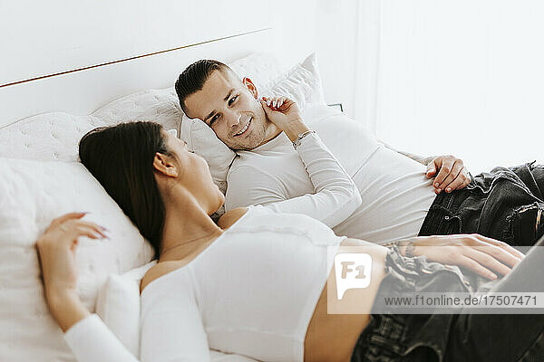 Smiling man resting with woman on bed at home