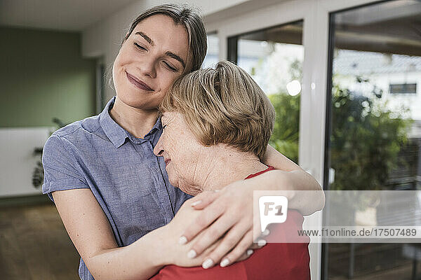 Smiling caregiver hugging senior woman at home
