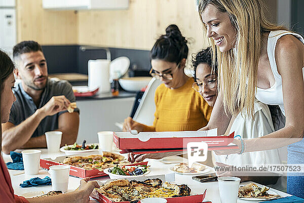 Smiling businesswoman with pizza box by colleagues in lunch break