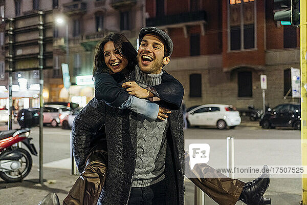 Cheerful boyfriend carrying girlfriend piggyback while walking in city