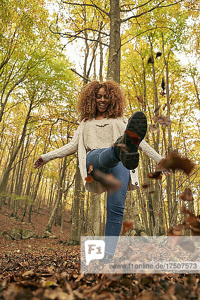 Happy woman kicking leaves in autumn forest
