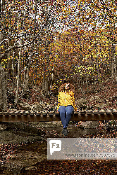 Woman relaxing on wooden bridge in autumn forest