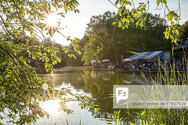 Germany  Bavaria  Munich  Sun setting over Mollsee lake in Westpark with beer garden in background