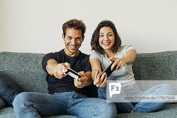 Cheerful young couple playing video game on sofa in living room