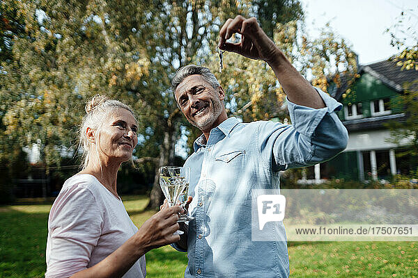 Lächelnder Mann hält Champagnerglas und Hausschlüssel von Frau im Hinterhof