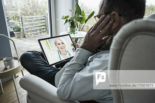 Smiling doctor on tablet PC screen talking with man at home