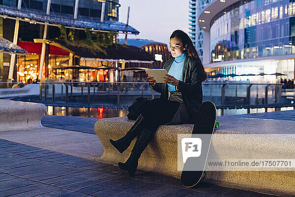 Working woman using tablet PC on bench in city