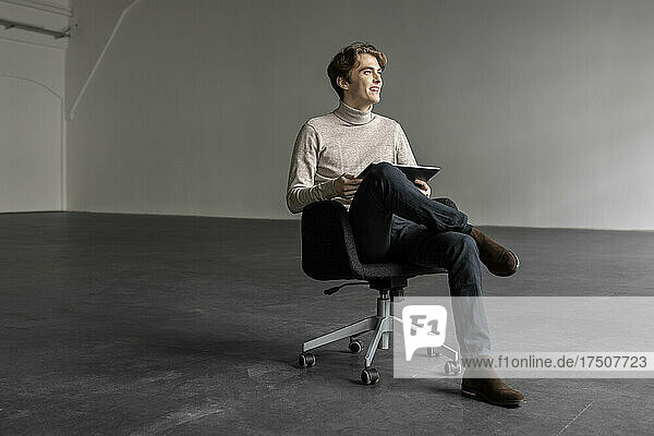 Young businessman with tablet pc smiling on chair at industrial hall