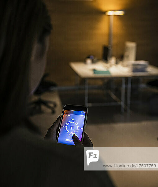 Woman using light bulb icon mobile phone screen at home