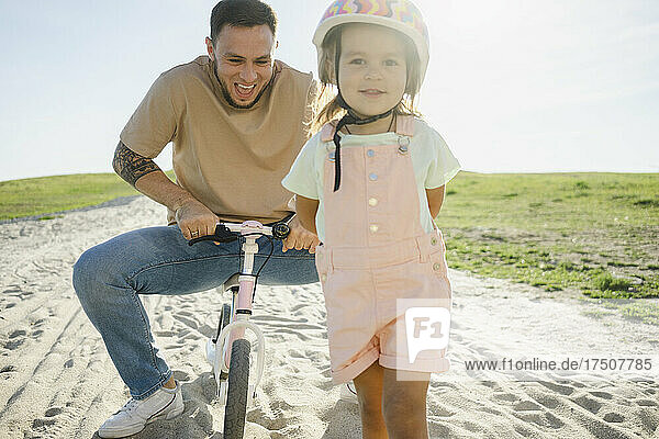 Girl with helmet with father sitting on bicycle in background