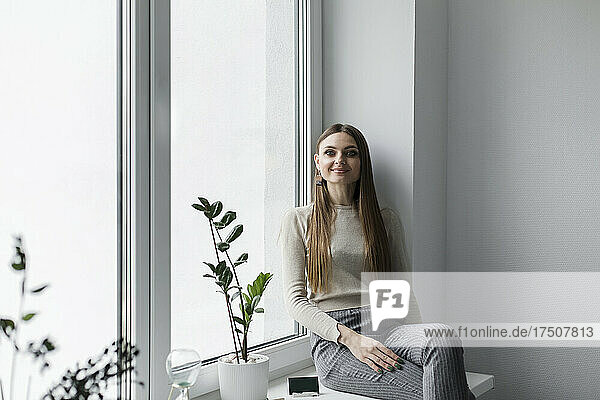Lächelnde Geschäftsfrau sitzt auf der Fensterbank im Büro